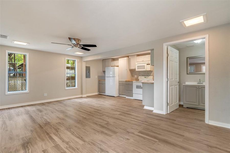 Unfurnished living room featuring ceiling fan, plenty of natural light, light wood-type flooring, and electric panel Unfurnished living room featuring ceiling fan, plenty of natural light, light wood-type flooring, and electric panel