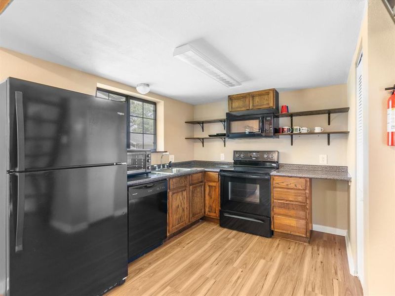 Kitchen with black appliances, open shelves, light wood-style flooring, and brown cabinets Kitchen with black appliances, open shelves, light wood-style flooring, and brown cabinets