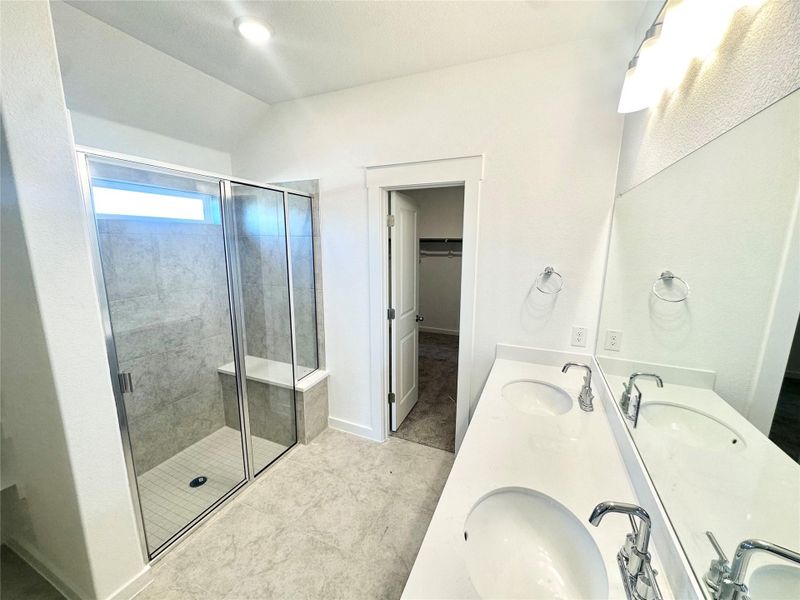 Full bath with a stall shower, double vanity, a walk in closet, and lofted ceiling