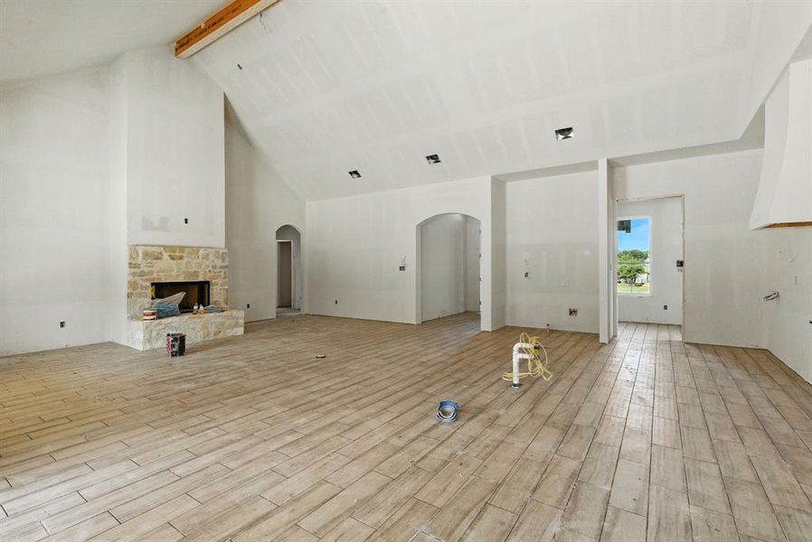 Unfurnished living room with beamed ceiling, light wood-type flooring, high vaulted ceiling, a fireplace, and arched walkways Unfurnished living room with beamed ceiling, light wood-type flooring, high vaulted ceiling, a fireplace, and arched walkways