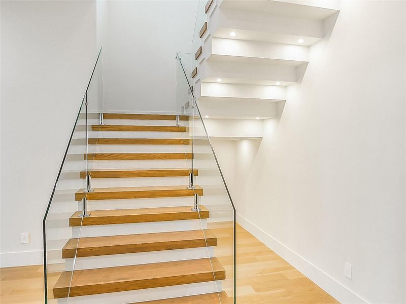 Modern staircase featuring light wood treads, a glass railing, and recessed lighting