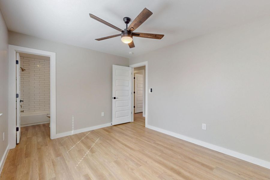 Unfurnished bedroom with light wood-style floors, baseboards, connected bathroom, and ceiling fan