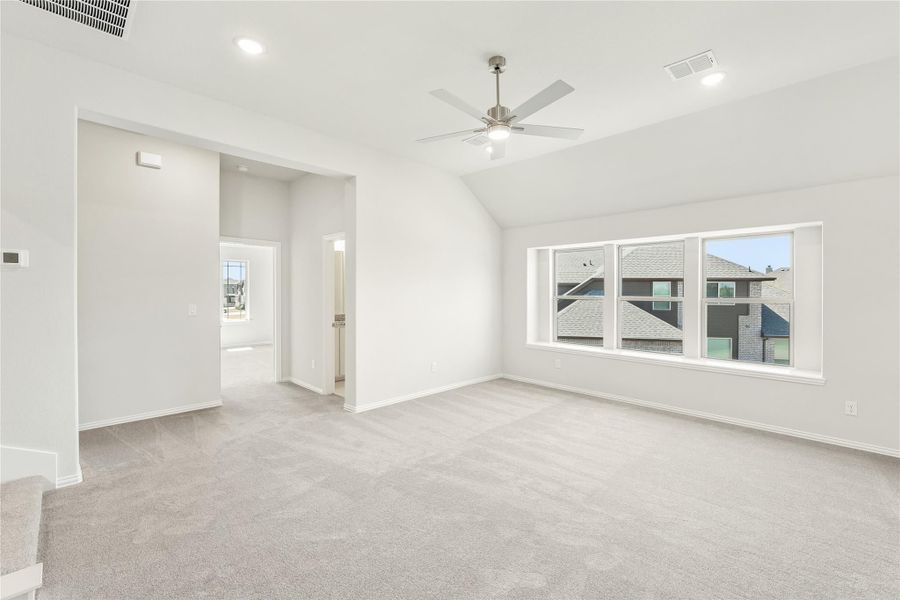 Empty bedroom with vaulted ceiling, ceiling fan, carpet flooring, and large windows overlooking neighboring homes
