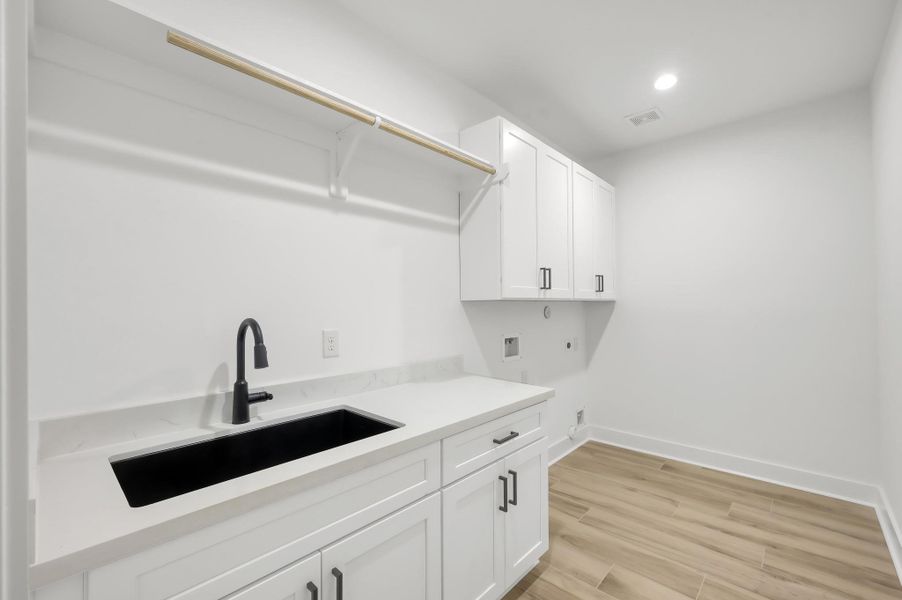 Oversized laundry room with built-in cabinetry, deep utility sink, quartz counters, and plenty of space for storage and organization.
