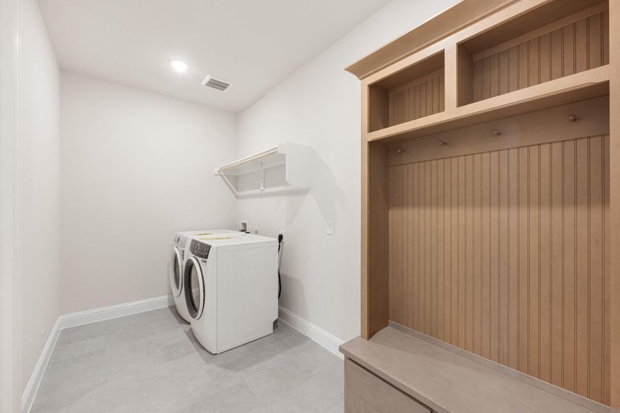 Laundry and mudroom combo with washer and dryer, built-in wood cubbies, bench, and wall shelf on tile floor