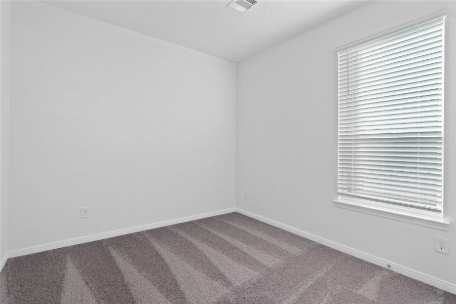 Secondary bedroom features plush carpet flooring, neutral paint, lighting, large window with privacy blinds, and an ample sized closet space.