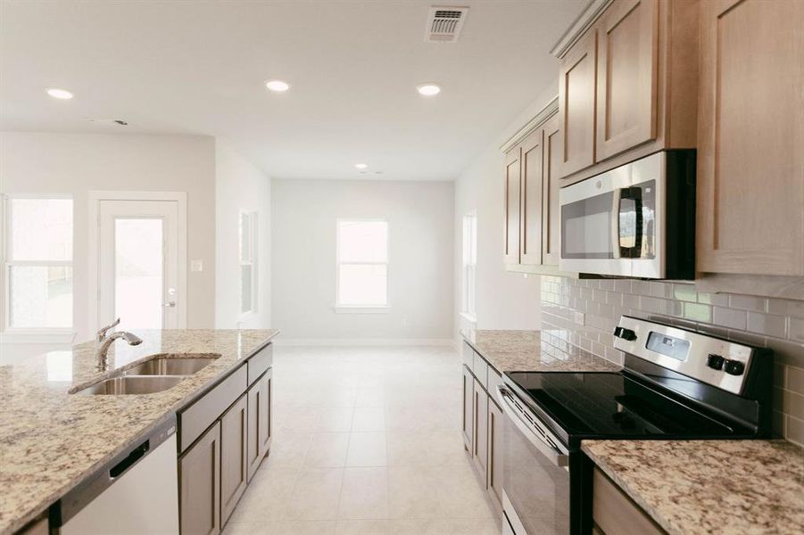 Kitchen with light tile patterned flooring, light stone counters, appliances with stainless steel finishes, decorative backsplash, and sink