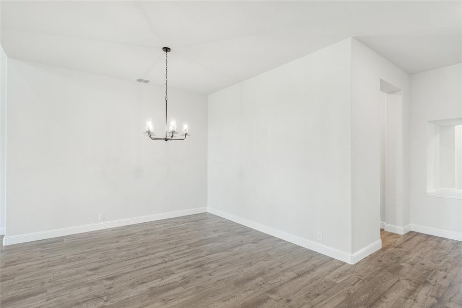 Empty dining room with wood-look floors, white walls, and a black chandelier overhead