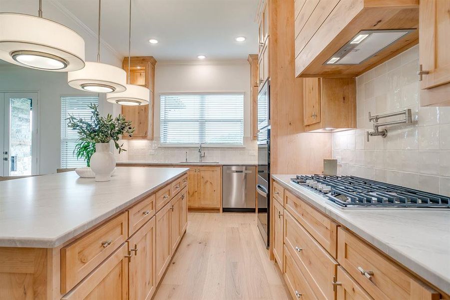Kitchen with custom Knotty Alder wood cabinets to the ceiling, leathered Quartzite counters, tile backsplash, decorative lighting, ample storage, soft close doors and drawers, and gas cooktop.