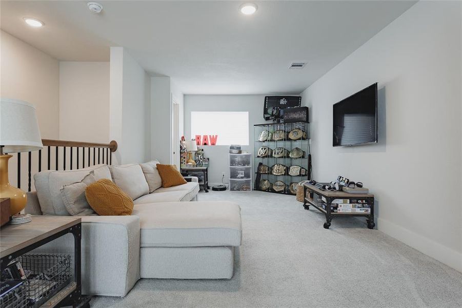 Carpeted loft area featuring a wall-mounted television, recessed lighting, and a window with horizontal blinds