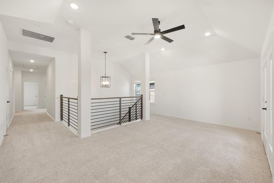 Open upstairs loft with vaulted ceiling, ceiling fan, carpet, and metal stair railing overlook