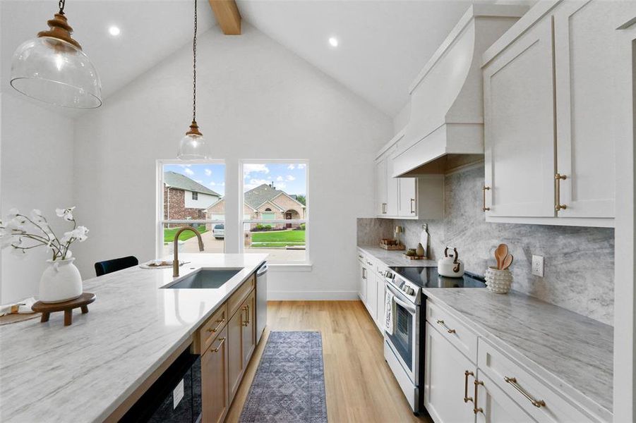 Kitchen with vaulted ceiling, wood-finish flooring, white cabinetry, integrated range hood, and a large central island featuring a sink and pendant lighting