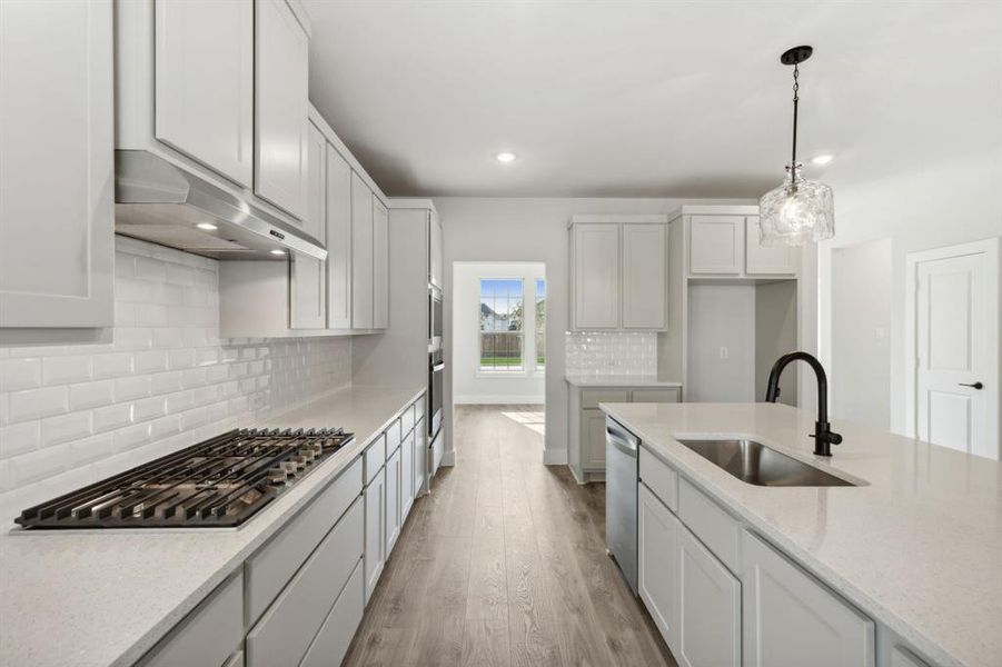 Kitchen featuring stainless steel appliances, sink, decorative light fixtures, white cabinets, and light wood-type flooring