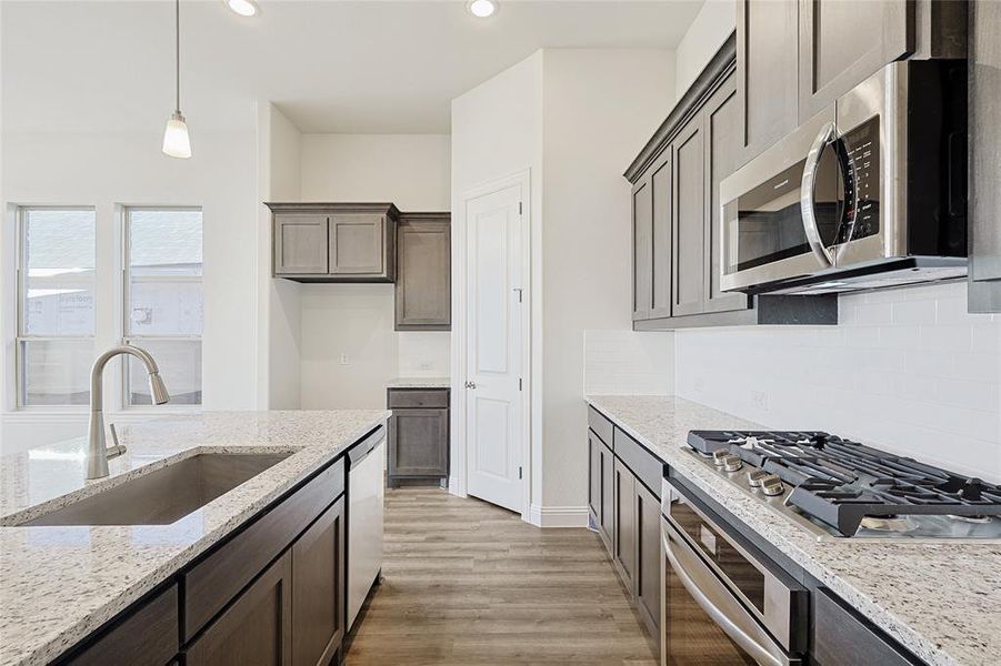 Kitchen featuring light stone counters, stainless steel appliances, sink, pendant lighting, and light hardwood / wood-style flooring