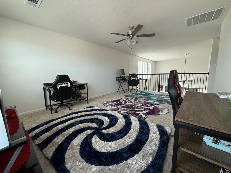 Versatile loft space featuring neutral carpeting, a ceiling fan, and white walls