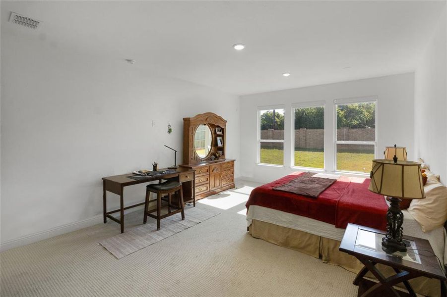 Bright bedroom featuring a trio of windows overlooking a landscaped backyard