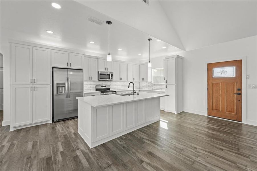 Kitchen with sink, white cabinetry, decorative light fixtures, appliances with stainless steel finishes, and an island with sink