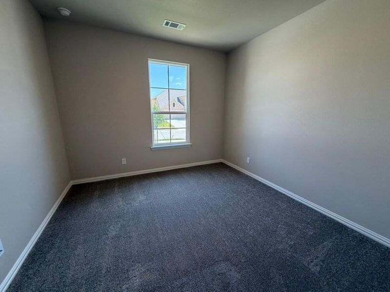 Spacious room featuring gray textured carpeting, neutral wall paint, white baseboards, and a single window with white trim