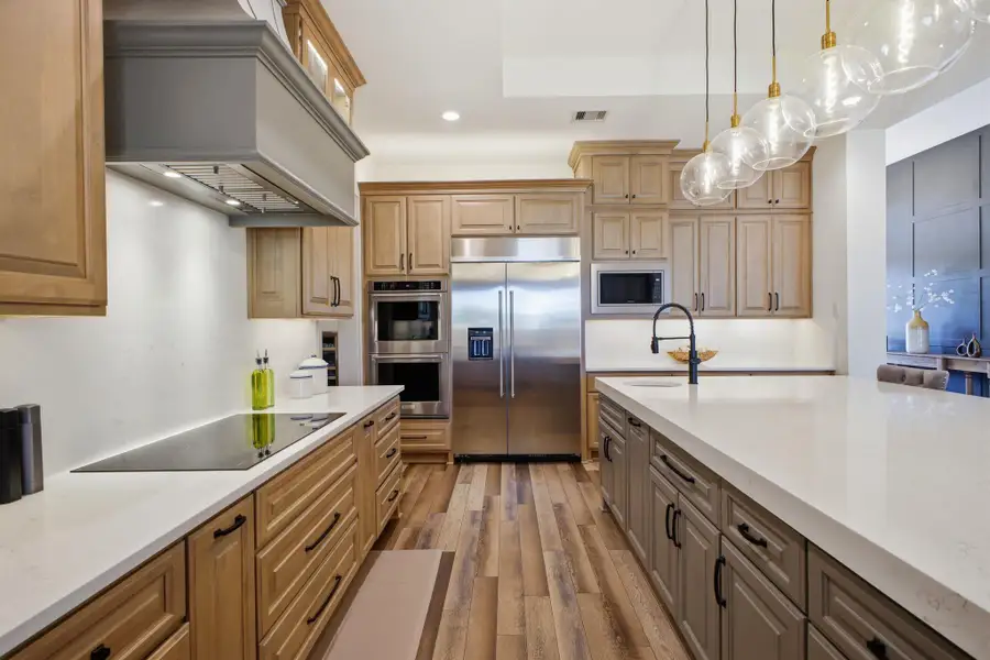 The kitchen features a large island with a sink and pendant lighting, stainless steel appliances, and extensive cabinetry with both light wood and grey finishes