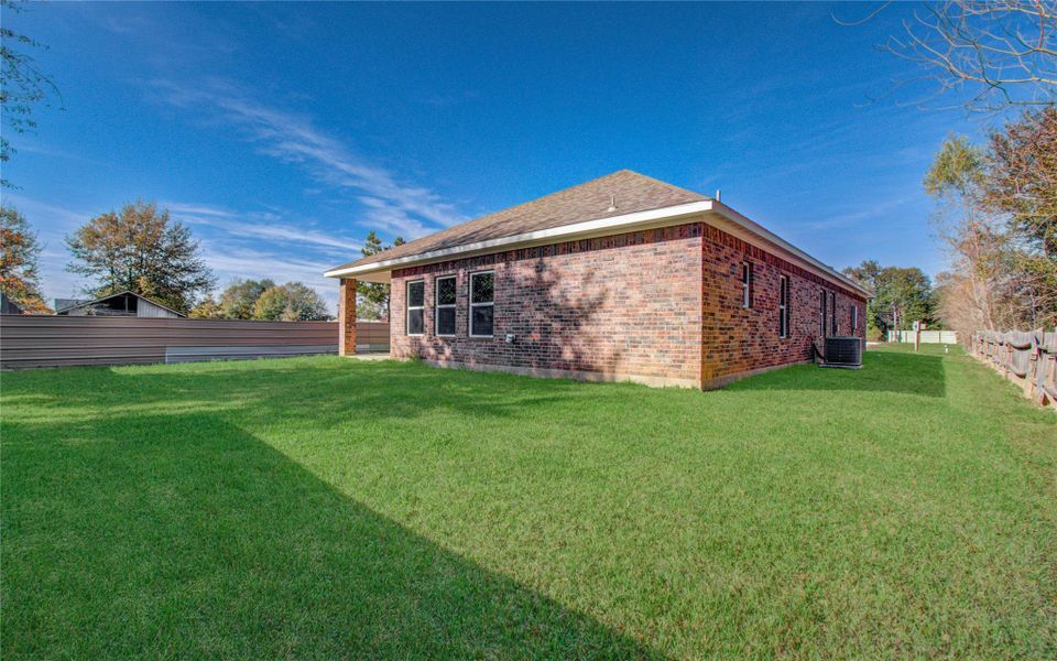 This photo shows a brick house with a spacious, well-maintained lawn. The property features a fenced backyard, providing privacy and a great space for outdoor activities. The clear blue sky adds to the welcoming atmosphere.