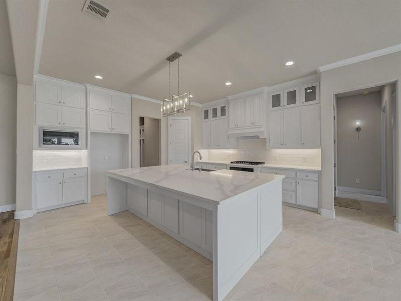 Kitchen featuring white cabinets, a center island with sink, glass insert cabinets, ornamental molding, and recessed lighting Kitchen featuring white cabinets, a center island with sink, glass insert cabinets, ornamental molding, and recessed lighting