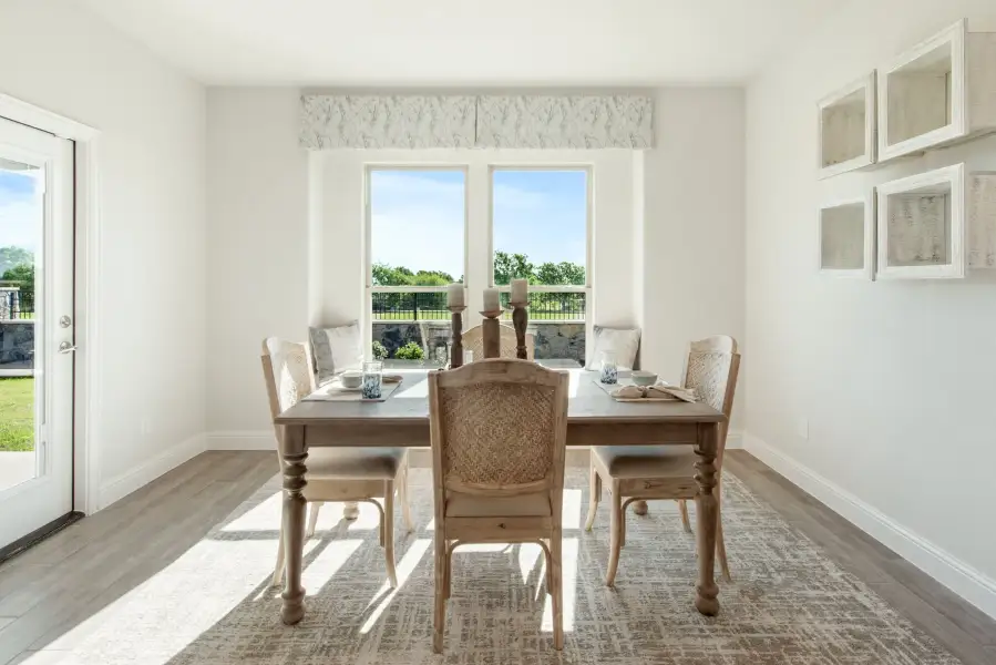 Bright dining room with wooden table, six chairs, hardwood floors, and large windows overlooking a backyard.