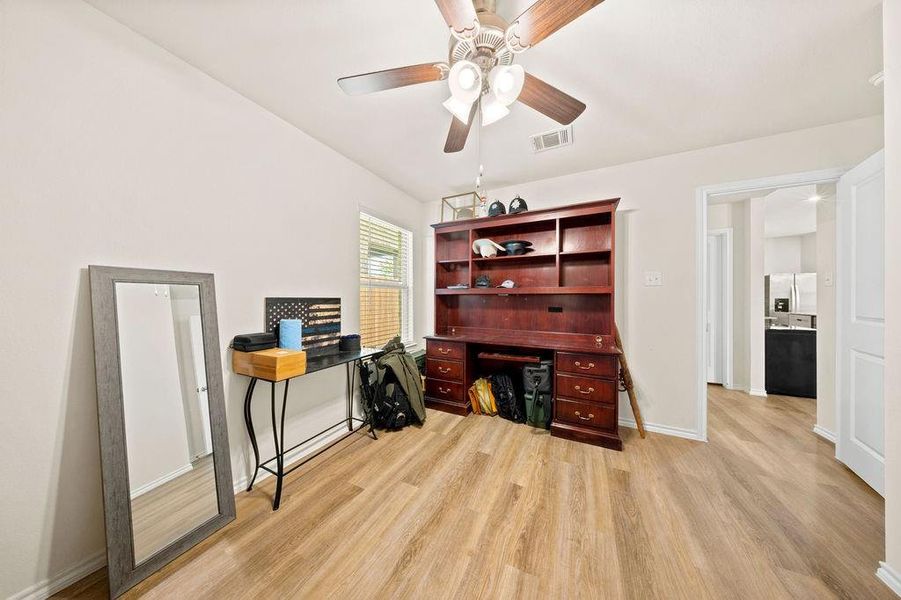Spacious room featuring wood-finish flooring, light neutral wall paint, and a ceiling fan with integrated lighting Spacious room featuring wood-finish flooring, light neutral wall paint, and a ceiling fan with integrated lighting