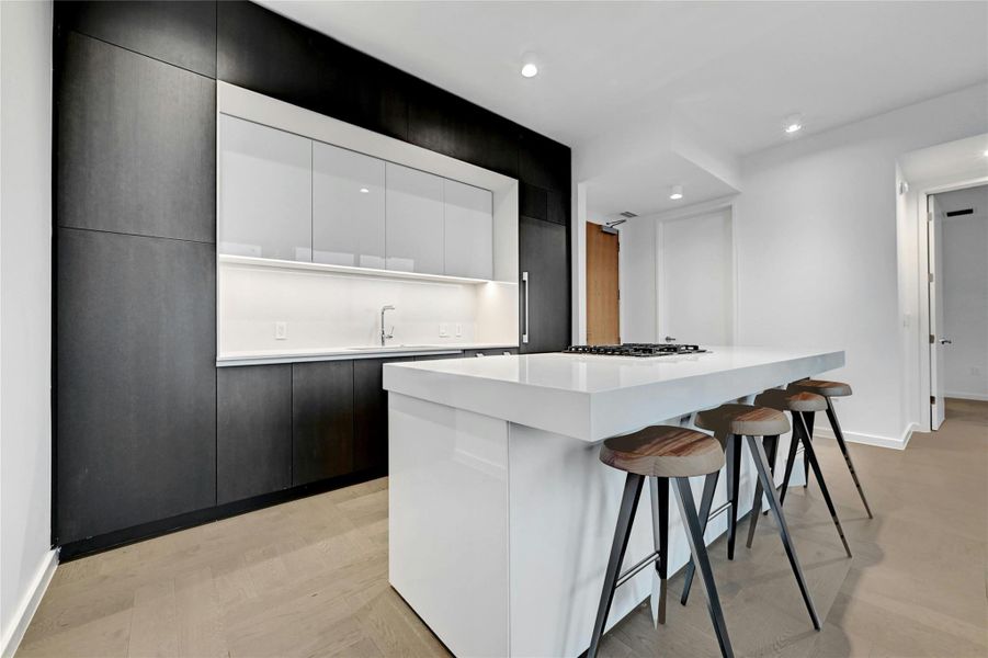 Sleek kitchen with integrated appliances, custom cabinetry and a large waterfall island with bar seating. Furnishings provided by Scott + Cooner available for purchase separately. Photo is model unit #2406.