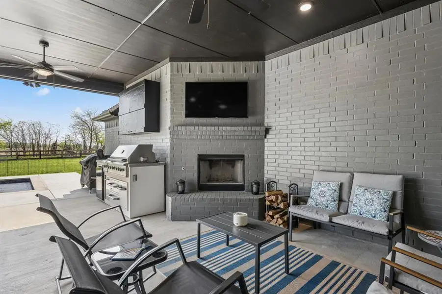 View of patio featuring ceiling fan, an outdoor brick fireplace, and an outdoor kitchen and area to lounge
