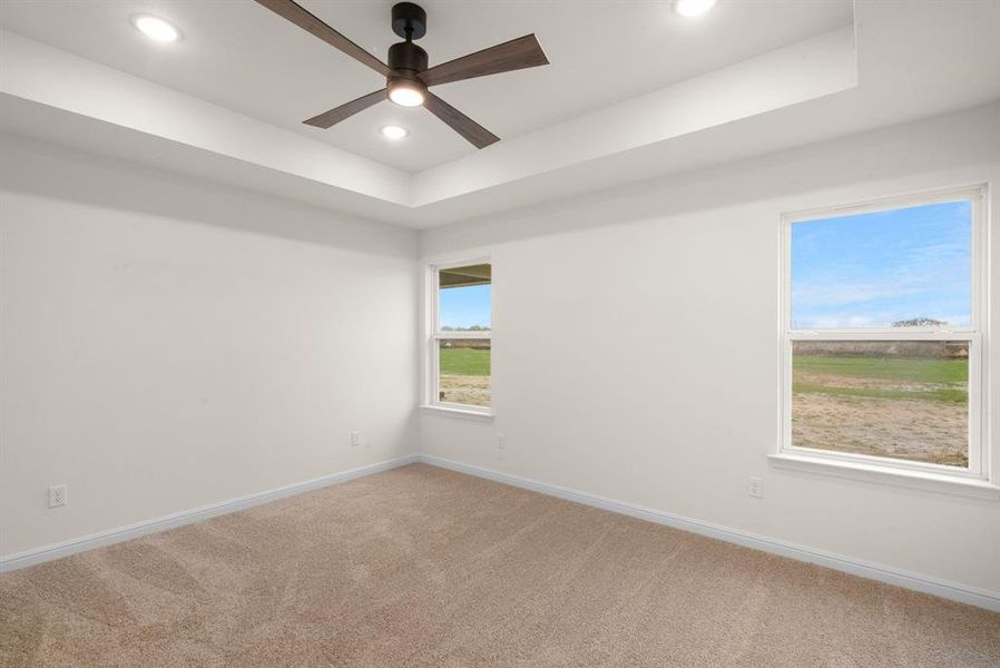 Empty room with carpet flooring, a raised ceiling, and ceiling fan Empty room with carpet flooring, a raised ceiling, and ceiling fan