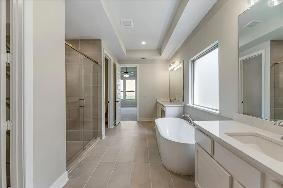 Bathroom with a shower stall, a freestanding bath, two vanities, light tile patterned floors, and ceiling fan