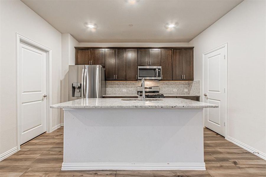 Kitchen featuring decorative backsplash, dark brown cabinets, appliances with stainless steel finishes, and a sink