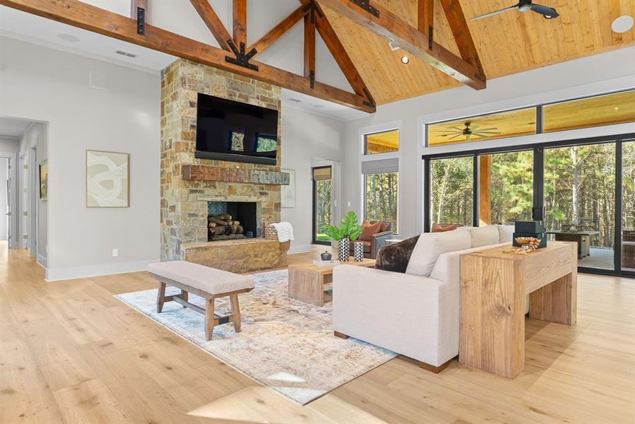 Living area with high vaulted ceiling, light wood finished floors, a stone fireplace, beam ceiling, and ceiling fan