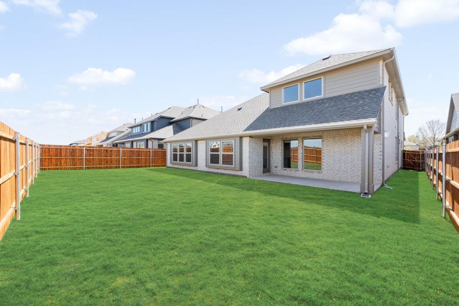 Backyard of two-story brick home with large green lawn, covered patio, and wood privacy fence.