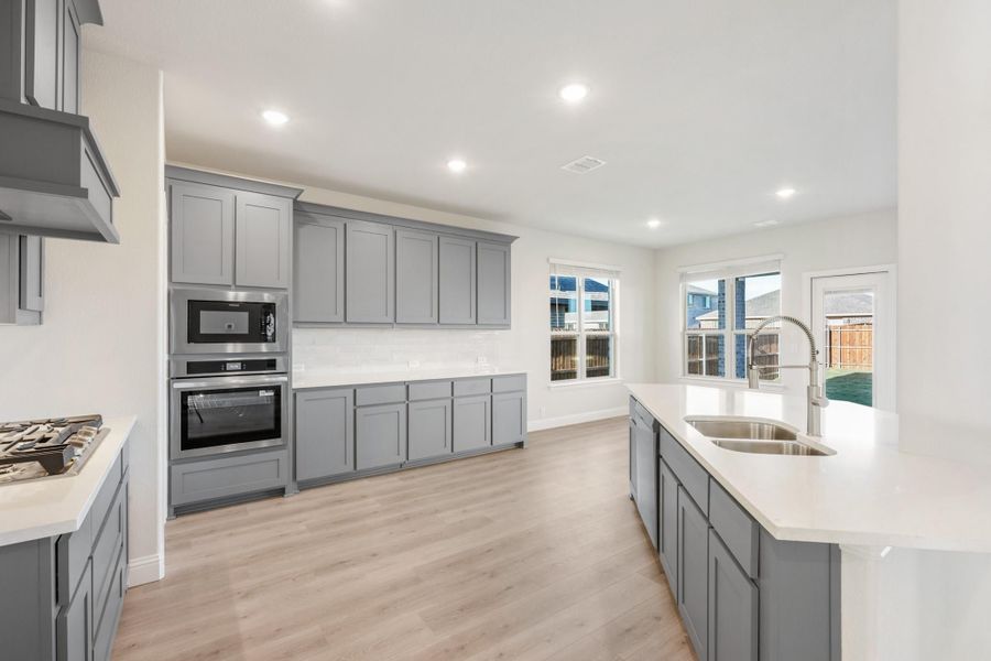Kitchen with gray cabinets, stainless steel appliances, island with sink, and light wood floors Kitchen with gray cabinets, stainless steel appliances, island with sink, and light wood floors