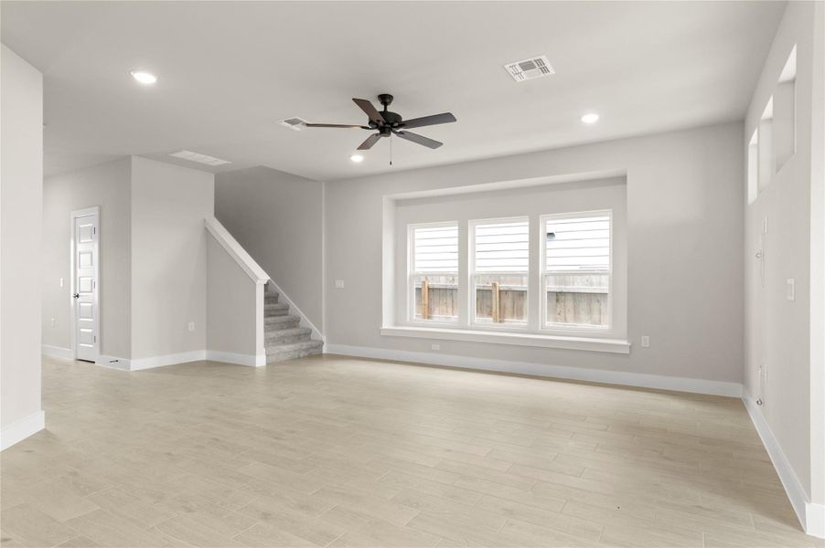 Unfurnished living room with ceiling fan, baseboards, stairs, light wood-type flooring, and recessed lighting Unfurnished living room with ceiling fan, baseboards, stairs, light wood-type flooring, and recessed lighting