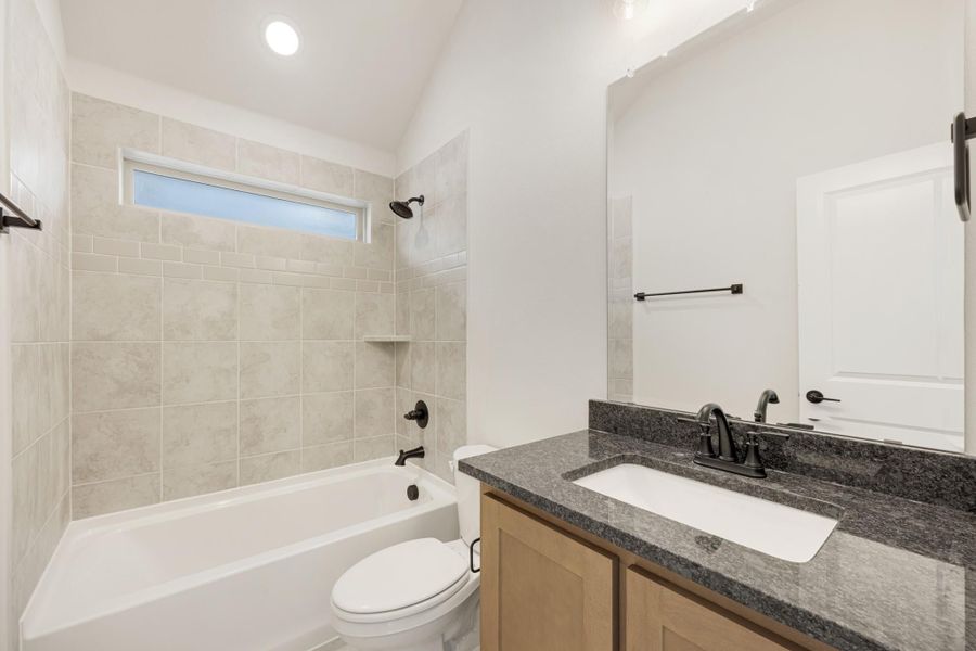 Bathroom with tiled tub-shower combo, granite vanity, wood cabinets, and vaulted ceiling
