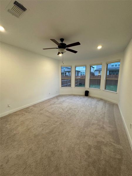 Expansive room featuring plush carpeting, a multi-pane bay window, and a ceiling fan with integrated lighting Expansive room featuring plush carpeting, a multi-pane bay window, and a ceiling fan with integrated lighting