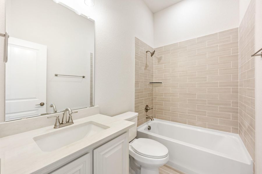 Bathroom with white vanity, single sink, toilet, and tub-shower combo with beige subway tile surround