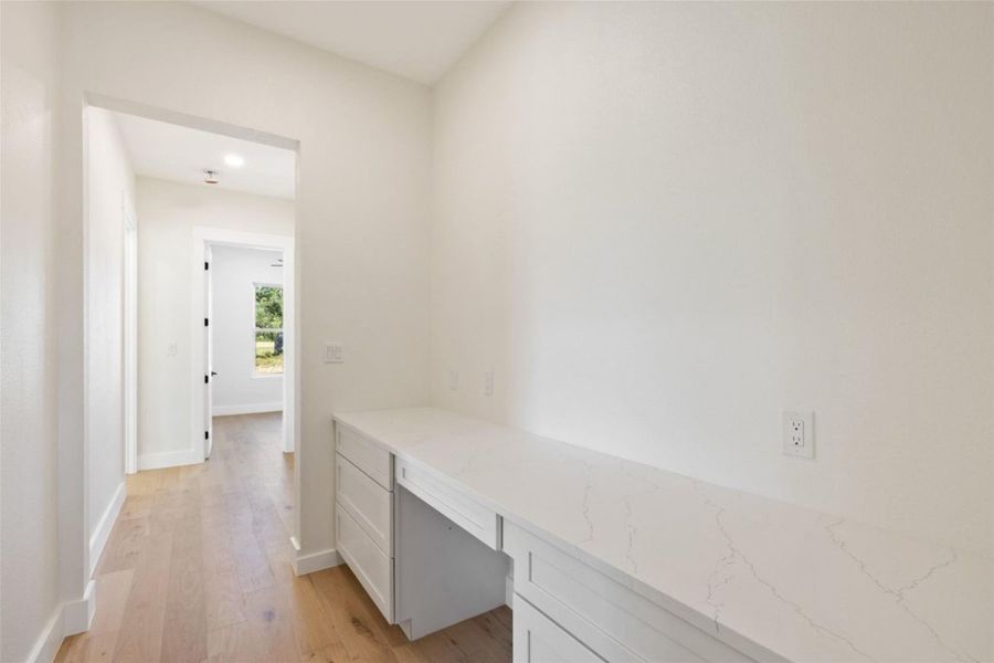 A well-lit hallway features built-in cabinetry, elegant countertops, and light wood flooring. A well-lit hallway features built-in cabinetry, elegant countertops, and light wood flooring.