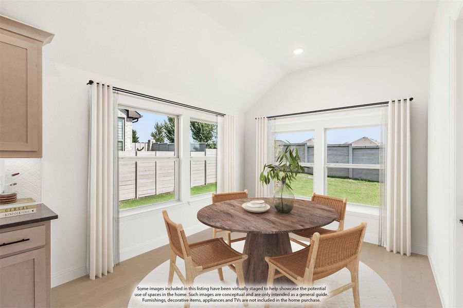 Bright breakfast nook with round wood table, four wicker chairs, vaulted ceiling, and large windows overlooking backyard