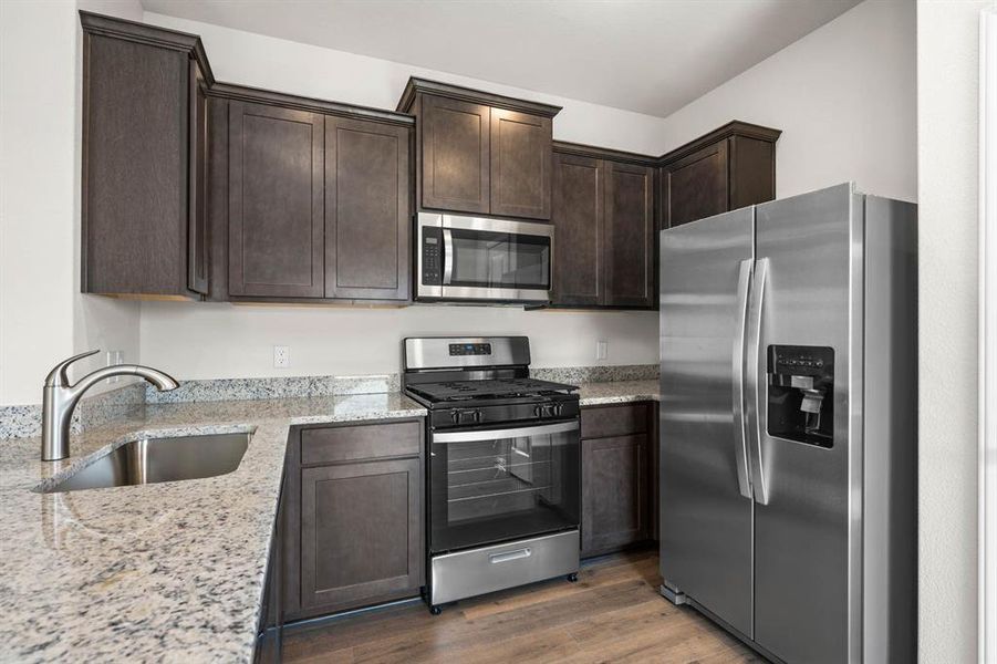 Kitchen with stainless steel appliances, light stone countertops, dark brown cabinets, and dark wood-type flooring