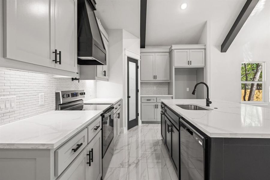 Kitchen with light stone counters, electric range, two tone color scheme, a kitchen island with sink, and light marble finish floors