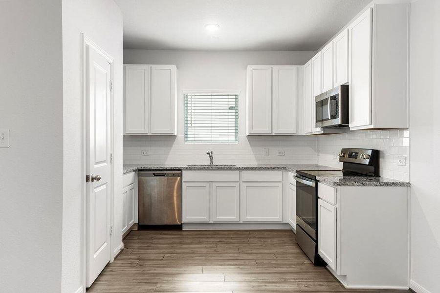 Kitchen with stainless steel appliances, light stone countertops, decorative backsplash, and white cabinets