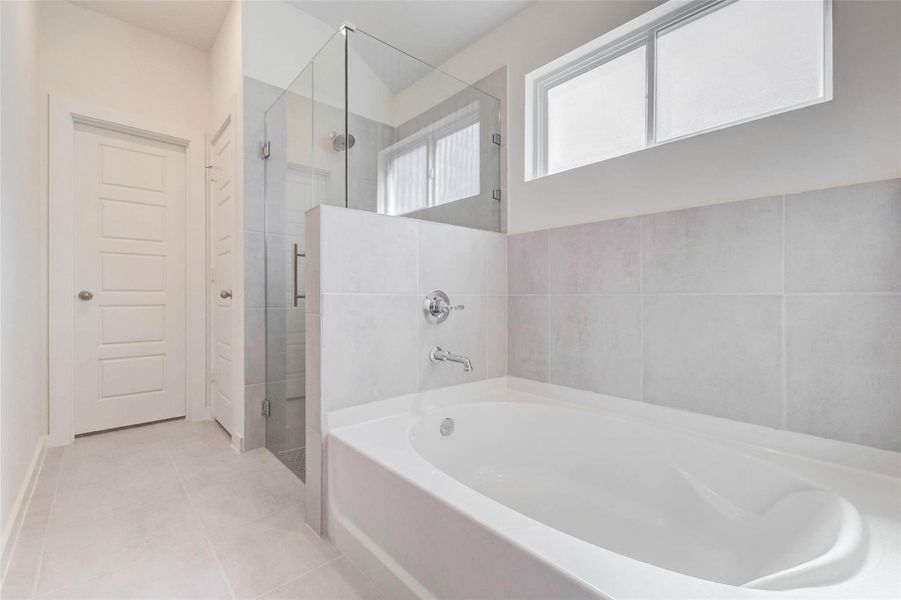 Primary bathroom featuring a soaking tub, separate glass-enclosed shower, neutral tile surround, high privacy window, and clean modern finishes. The layout offers a relaxing bath area with a separate shower zone, creating a comfortable and practical en-suite retreat.