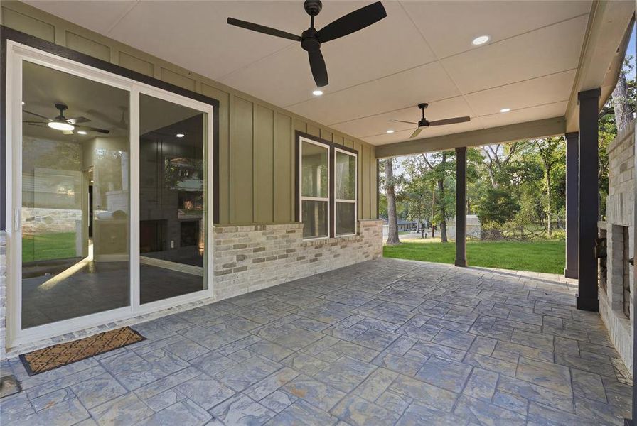 Expansive covered patio featuring stamped concrete flooring, multiple ceiling fans with integrated lighting, recessed lighting, and a stone-clad outdoor fireplace Expansive covered patio featuring stamped concrete flooring, multiple ceiling fans with integrated lighting, recessed lighting, and a stone-clad outdoor fireplace