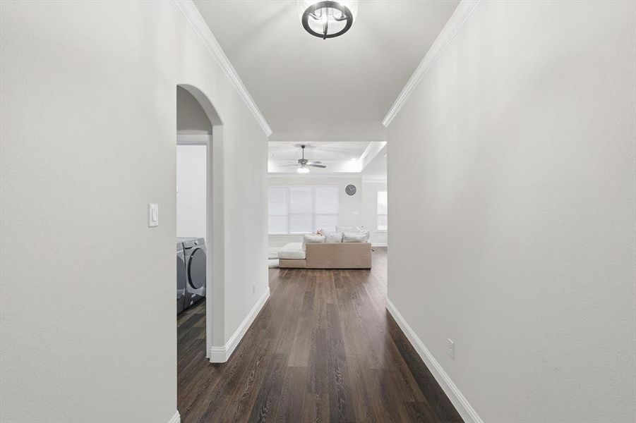 Hallway with ornamental molding, independent washer and dryer, dark wood-type flooring, and arched walkways
