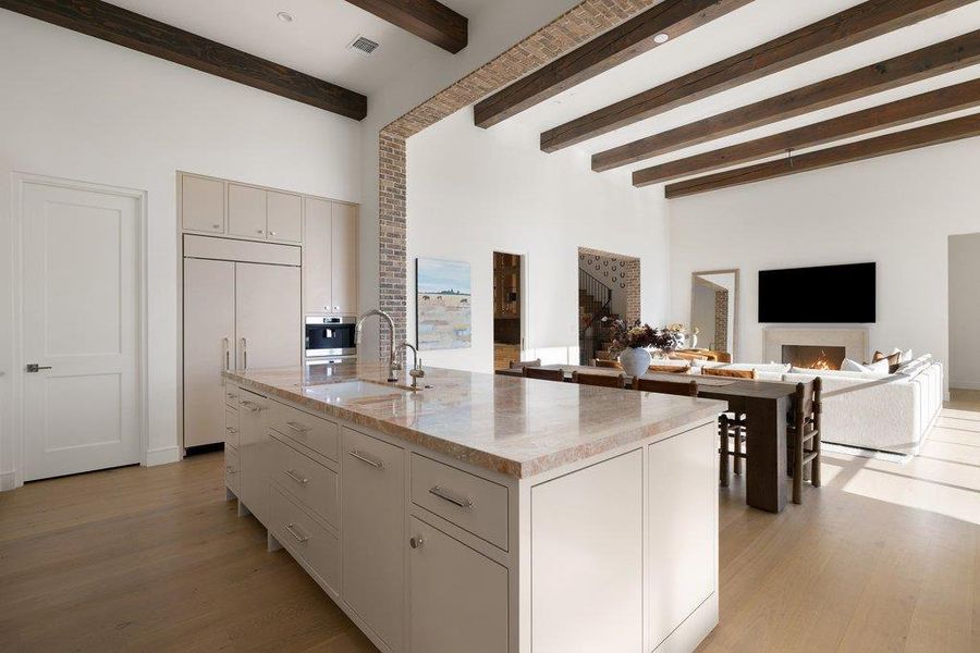 Kitchen featuring open floor plan, light stone counters, a center island with sink, paneled built in refrigerator, and light wood-style flooring