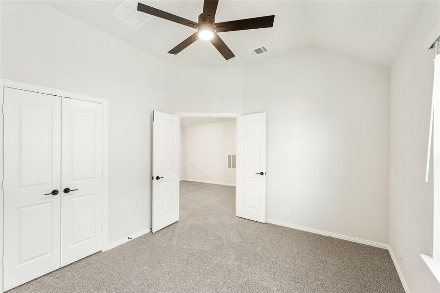 Empty bedroom with gray carpet, ceiling fan, double closet doors, and open double doors to hallway Empty bedroom with gray carpet, ceiling fan, double closet doors, and open double doors to hallway
