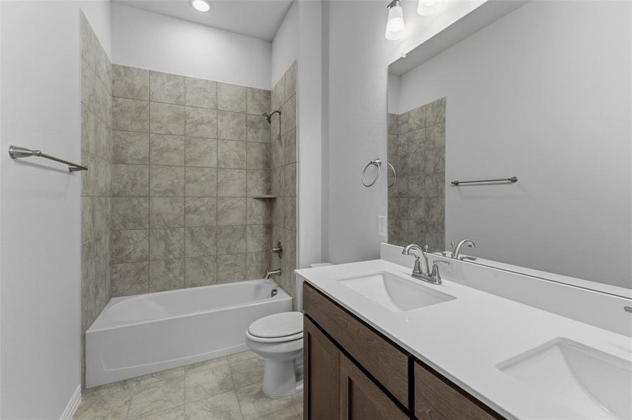 Bathroom featuring a dual vanity with integrated sinks and white countertops, dark wood-finish cabinetry, a large mirror, and a bathtub with a tiled shower surround